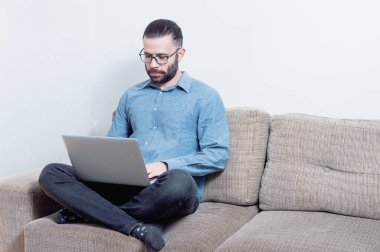 Evde çalışan genç bir adamın fotoğrafı. Bir vagonda oturuyor ve mavi gömlek giyiyor.