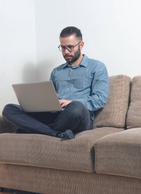 Evde çalışan genç bir adamın fotoğrafı. Bir vagonda oturuyor ve mavi gömlek giyiyor.