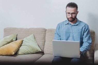 Evde çalışan genç bir adamın fotoğrafı. Bir vagonda oturuyor ve mavi gömlek giyiyor.