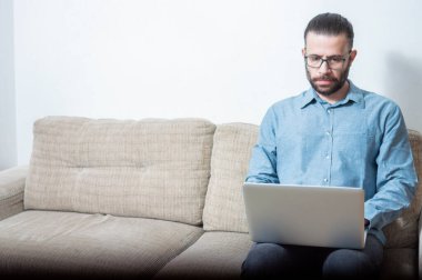 Evde çalışan genç bir adamın fotoğrafı. Bir vagonda oturuyor ve mavi gömlek giyiyor.