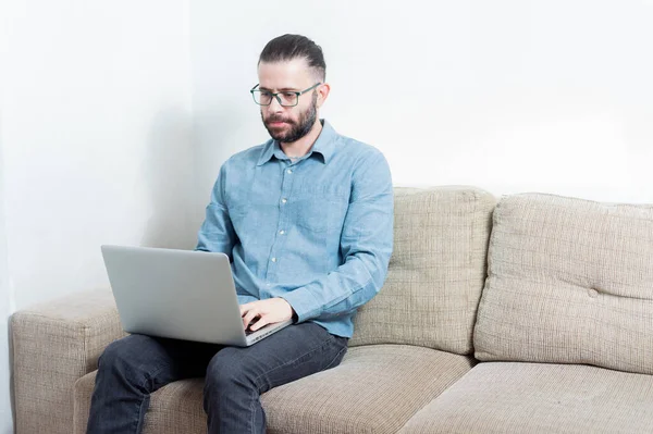 Evde çalışan genç bir adamın fotoğrafı. Bir vagonda oturuyor ve mavi gömlek giyiyor.