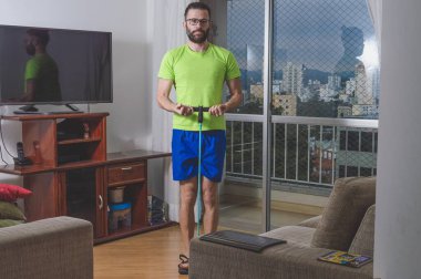 Evde yeşil gömlek ve mavi şort giyen genç adamın portresi.