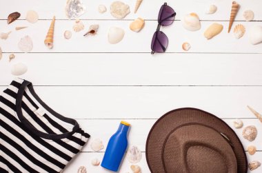 Üst Manzara. Aksesuarlar yaz tatili konsepti, beyaz gömlekli plaj güneş gözlüğü krem şapka, çanta kotu ve beyaz ahşap masa üzerinde deniz kabuğu kopyalama alanı.
