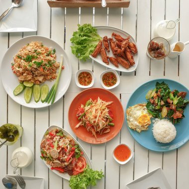 Tavuklu pilav, yumurta, sebze, papaya salatası kızarmış tavuk ve kızarmış kale, beyaz ahşap masada Tayland domuz salatası.