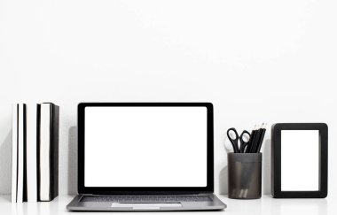 Boş ekranı ve kitabı olan dijital teknoloji dizüstü bilgisayarı, beyaz ahşap masadaki resim çerçevesi, ev içi veya ofis arka planı