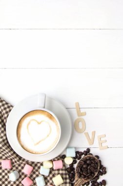 Kahve fincanı beyaz hardal latte sanat ve marshmallow tatlı, kavrulmuş kahve çekirdekleri beyaz ahşap, metin için boşluk kopyala.