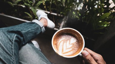 Kotlar ve beyaz spor ayakkabılar giyen, sağ koltukta oturan, sabahın köründe kafede eğreltiotu yaprağıyla kahve içen biri.