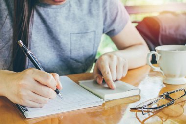 Asyalı genç bir iş kadını ya da öğrenci elinde kalemle kağıda bardaklarla, masaya kahve yazarak mektup yazıyor..