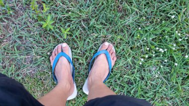 Yeşil çim arka planda mavi beyaz terlik giyen bir adam.