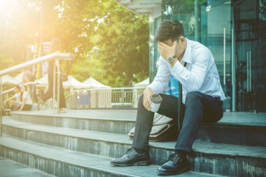 Asian businessman Wearing white shirt sitting stress unemployed on staircase with work  sunset background. clipart