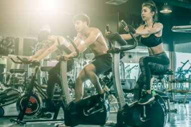 Genç Asyalı erkek ve kadınlar. Spor salonunda bisiklet sporu, gün batımında grup spor, hafif odaklanma.