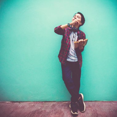 Odaklan, bulanık Asyalı genç adam. Gözlerini kapat. Kitap kulaklıkları yeşil duvarda, kare kompozisyonda müzik dinliyorlar.