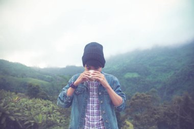  Hafif bulanık, İskoç gömlekli ve siyah şapkalı Asyalı genç bir kadın bulutların tepesinde sıcak kahve içiyor ve dışarıda sis Hiker var. Doi Luang Chiang Dao Chiangmai Eyaleti, Sabah.