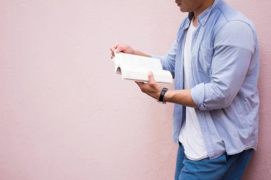 Mavi gömlekli ve gözlüklü yakışıklı bir Asyalı. Siyah gözlüklü. Pembe arka plan parkında durmuş kitap okuyor ve rahatlıyor. Seçici Odaklanma.