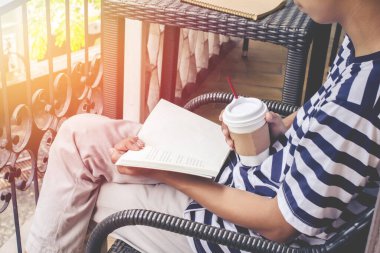 Genç adam antika sandalyede oturmuş elinde kahve içiyor ve günbatımında hafif bir tonda kitap okuyor.