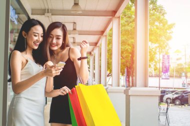 Beyaz ve siyah elbiseli güzel Asyalı kadınlar ellerinde telefon, alışveriş torbaları sokak şehrinde eğleniyorlar. Alışveriş Konsepti