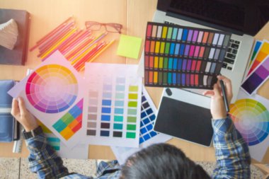 Görüntü, Üst Görüntü. İskoç gömlekli tasarımcı, Mouse kalem tutan grafiksel yaratıcı ve ofiste dizüstü bilgisayar üzerinde çalışan, Sunset arka plan, Seçici odak.