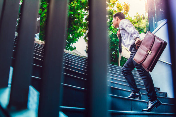 Молодой азиатский бизнесмен, держащий коричневую кожаную сумку, работающую на лестничной клетке идти в офис спешите рабочее время с закатом вид сверху и Instagram стиле фильтр фото винтажный тон