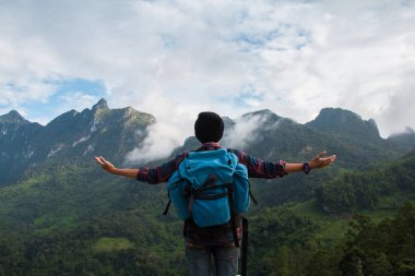İskoç gömlekli ve siyah şapkalı Asyalı genç adam bulutların tepesinde ve dışarıda sis yürüyüşünde kollarını açmış mutlu bir şekilde dikiliyor. Doi Luang Chiang Dao Chiangmai Eyaleti, Sabah.
