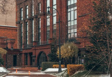 Güzel tuğla bina. Bina girişi. Sonbahar ve kış arasında. Kar yağıyormuş. Sarı yapraklar. Güzel bir fener. Kış tatili atmosferi. Noel ve Yeni Yıl.