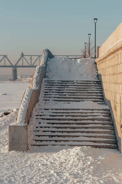 Stairs of the city embankment littered with snow. Industrial landscape. The atmosphere of frost, winter and snow.