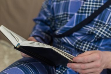 Mavi çizgili sabahlıklı bir adam kitap okuyor. Ev ortamı. Dikkatimi dağıttı. Kağıt kitap. Adam kanepede oturuyor..