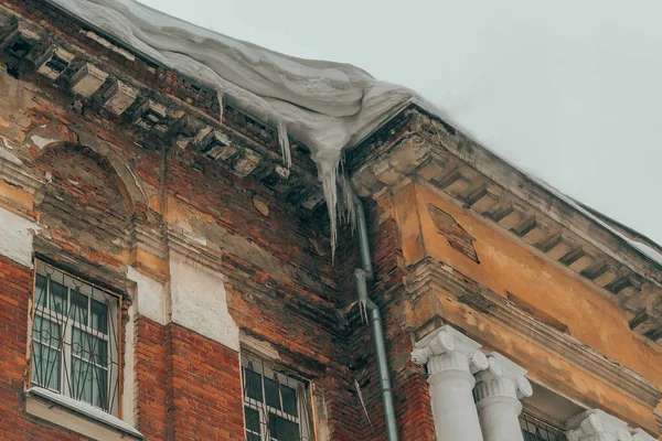 Corner of an old brick building. Snow on the roof, icicles. Crumbling building, old facade