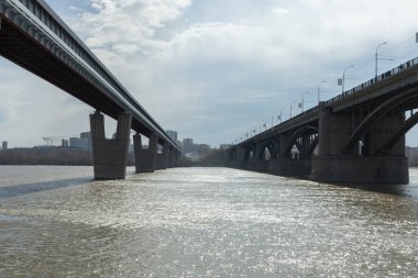 Şehir manzaralı iki köprü. Bahar, bulutlu hava. Diğer kıyıya. İnşaat halindeki bir şehir.
