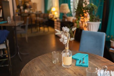 Konforlu bir evde yemek masası. Masada suni çiçekler var. Masadaki çatal bıçak takımı.