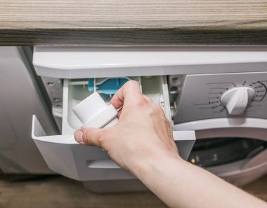 El çamaşır makinesine deterjan ekler. Evde çamaşırhane. Ev işleri..