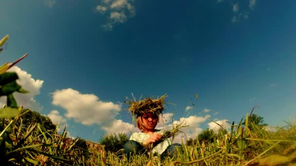 Fair-haired daughter of a farmer weaves a wreath made of straw — Stock Video