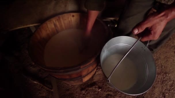 Hand häller ett glas mjölk från en trä fat i en hink bergsstil — Stockvideo