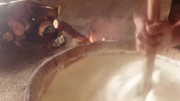 Farmer batters hot fermented sheep's milk in a wooden mortar on a background of fire — Stock Video