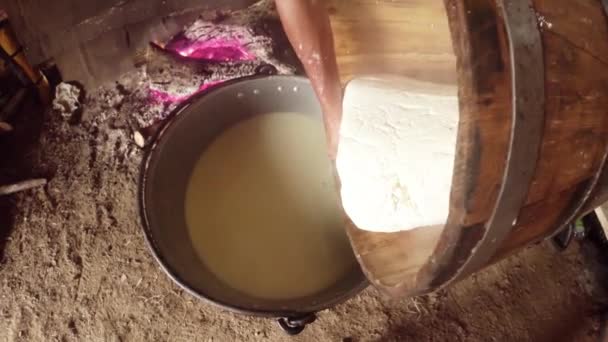 La mano presiona el queso de oveja en una tina de madera en el fondo de una hoguera — Vídeos de Stock