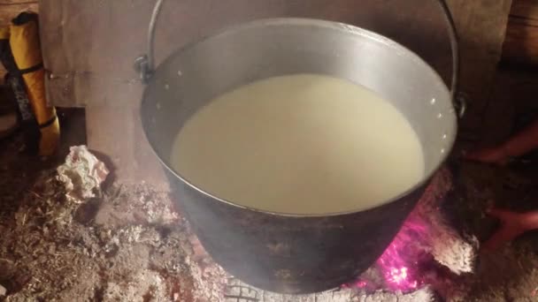 Fårmjölk kokt i en järngryta över en eld mitt i trähus av herdar — Stockvideo