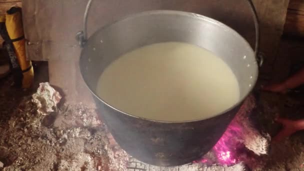 Leche de oveja cocinada en una olla de hierro sobre un fuego justo en la casa de madera de los pastores — Vídeos de Stock