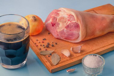 Çiğ domuz budu, sarımsak, soğan, kurutulmuş defne yaprakları, ahşap kesim tahtasındaki deniz tuzu ve biberler..