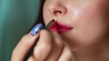 Makyaj sanatçısının eli ince bir fırçayla uygulanır ve genç ve güzel bir kadının dudaklarına ruj sürer. Gülümseyen kadın