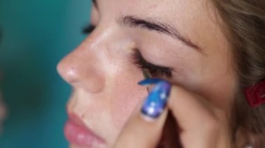 Makyajcı kızın kirpiklerine küçük bir fırça sürerek özel bir alet uygular.