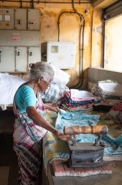 Geleneksel giysili kadın elinde antika bir kömür ütüsüyle, Dhobi Ghat, Kochi, Hindistan 'da açık hava çamaşırları, 20 Mart 2025
