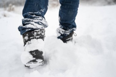 Kışın taze karlar içinde botlarla yürümek, kar taneleriyle kaplı kot pantolon ve ayakkabılar, kışın soğuk, fırtınalı hava koşulları