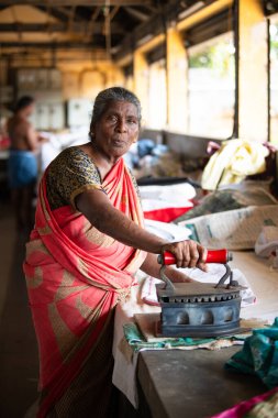 Geleneksel giysili kadın elinde antika bir kömür ütüsüyle, Dhobi Ghat, Kochi, Hindistan 'da 29 Mart 2025' te hava çamaşırhanesini açıyor.