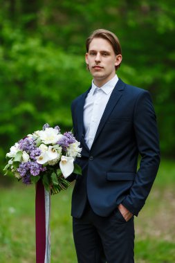 Genç güzel damat ayakta ve düğün buket holding