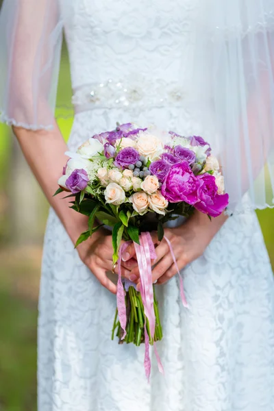 Noiva em um vestido branco no parque verde de verão com um buquê de casamento em mãos — Fotografia de Stock