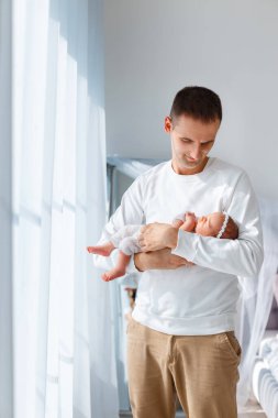 Beyaz takım elbiseli yeni doğmuş bebek babasının ellerinde uyur. Baba ve kızı. Kafasında saç bandı olan küçük bir çocuk. Mutlu ebeveynlik kavramı, aile ve çocuk bakımında sevgi