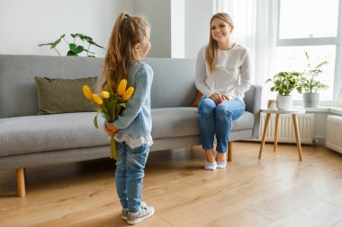 Uluslararası Kadınlar ve Anneler Günü. Bir buket sarı çiçekli şirin kız, gülümseyen annesini tebrik ediyor. Mutlu aile tatilleri. Kıvırcık kız sürpriz anne