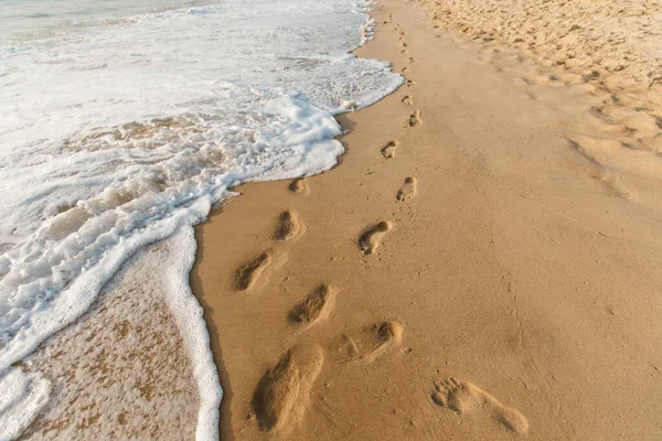 Two footprints ways on the sand. Ocean waves wash away people's tracks. Concept of honeymoon and walking on the summer beach