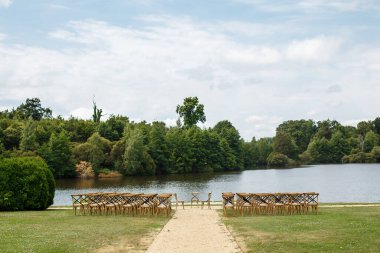 Gölün arka planında düğün töreni. Fransa Şatosu 'nun bahçesindeki çimlerin üzerinde duran misafirler için ahşap sandalyeler. Açık hava kutlaması için güzel bir yer.