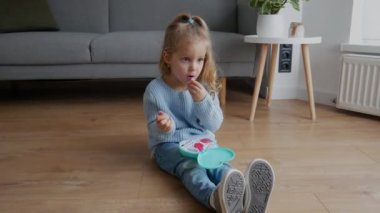 Küçük kız dudaklarını bebek rujuyla boyuyor. Sevimli çocuk evde oyuncak kozmetikleriyle makyaj yapıyor. Mutlu çocukluk kavramı, çocuk eğlencesi