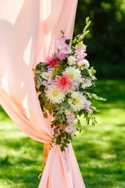 Parktaki düğün merasiminin yapılacağı yer. Tahta dikdörtgen kemer, çiçeklerle süslenmiş beyaz sandalyeler, yeşillik, taç yaprakları, şeftali rengi tül. Sevimli, modaya uygun kırsal dekor